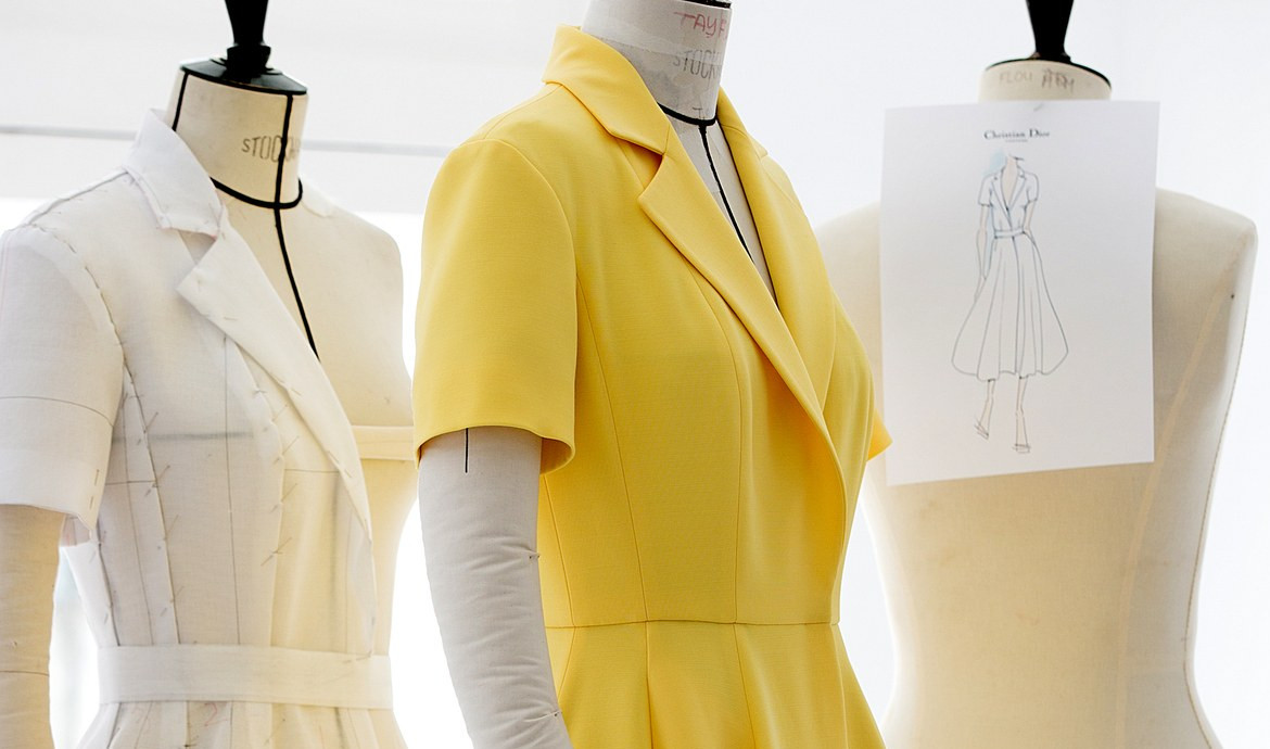 Une image montrant trois bustes de travail, un tailleur jaune manche courte au milieu, un tailleur en construction à gauche et un dessin de mode robe à droite.