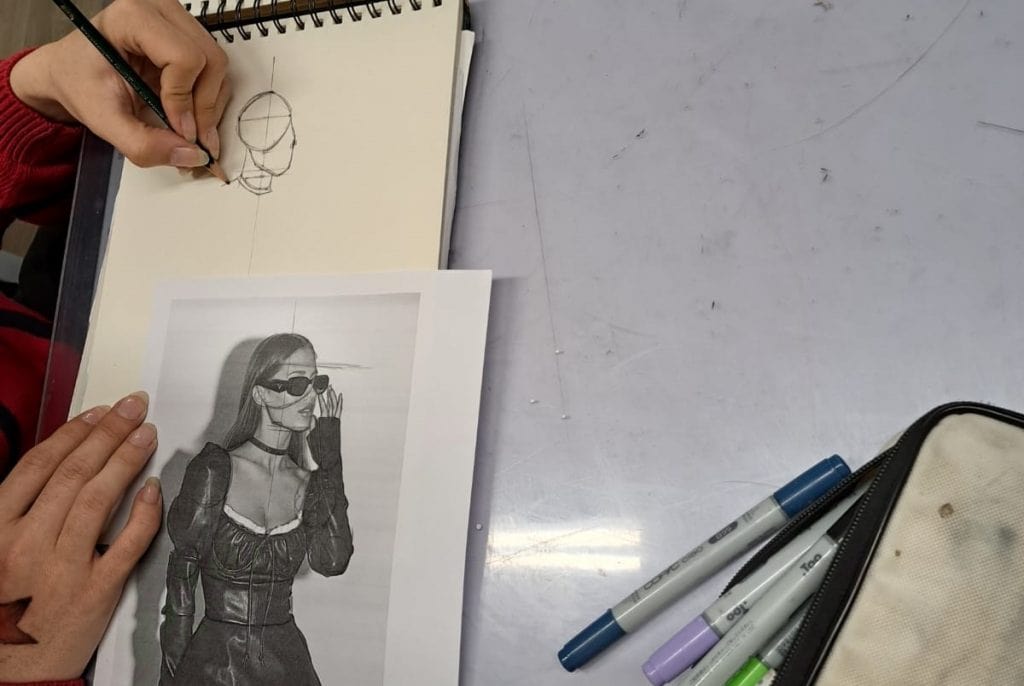 Étudiant en train de dessiner un croquis de mode à partir d'une photo de référence lors d'un cours de modélisme.
